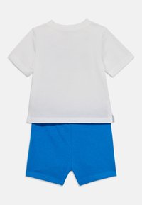 Λευκό βαμβακερό T-shirt με κοντό μανίκι, συνδυασμένο με μπλε βαμβακερές βερμούδες. Απλός σχεδιασμός, χωρίς ορατά μοτίβα ή αξεσουάρ.