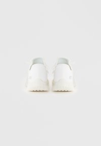 Baskets de sport blanches avec une tige en textile lisse, une forme arrondie et une semelle en caoutchouc texturée. Présente un marquage minimal sur le talon.
