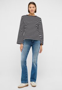 Pikkade varrukatega must-valgete triipudega top, kombineeritud heleroheliste laiade teksade ja beežide tossudega, modellil neutraalse taustaga.