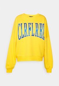Sudadera amarilla de gran tamaño con cuello redondo. Presenta letras azules en negrita que dicen "CLRFLRBL." Tela suave, puños y dobladillo elásticos.