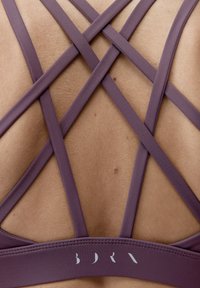 Purpurowy biustonosz sportowy z krzyżującymi się paskami na plecach, o gładkiej fakturze materiału i logo marki na gumie.