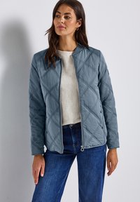 Pikowana jasnoniebieska kurtka z zamkiem z przodu, okrągłym dekoltem i guzikami po bokach. Wykonana z gładkiego materiału w diamentowy wzór, o luźnym kroju.