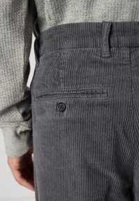 Grijze corduroy broek met verticale ribbels, met een enkele achterzak met een ronde zwarte knop en een gladde tailleband.