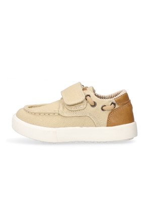 Zapato de lona beige con un acento de cuero marrón, tiras de Velcro y punta redondeada. Presenta una plantilla acolchada y una suela de goma texturizada.