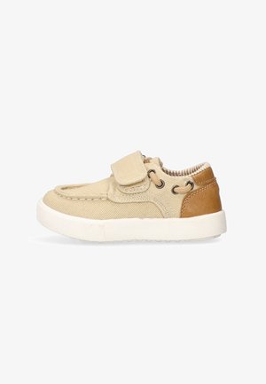 Zapato de lona beige con un acento de cuero marrón, tiras de Velcro y punta redondeada. Presenta una plantilla acolchada y una suela de goma texturizada.