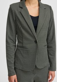 Juodas ir baltas houndstooth raštas švarkas su notch apykakle, vienu mygtuku ir priekinėmis kišenėmis. Pagamintas iš tekstūruoto audinio.