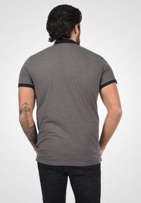 Polo-shirt gris à manches courtes avec un petit motif à pois, col noir et finitions noires sur les manches. Matière en coton, coupe standard, vu de dos.