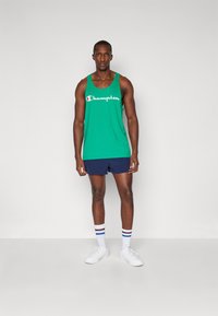 Grøn bomulds tanktop med hvid "Champion" logo, parret med marineblå shorts. Inkluderer hvide sko og stribede sokker i rød, hvid og blå.