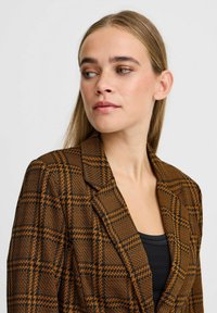 Brown and black checked blazer with a structured design, lapel collar, and textured fabric. Features a single-button closure and fitted silhouette.