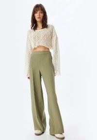 Top cropped au crochet blanc avec un motif en losanges ouvert, associé à un pantalon large olive. Tissu léger, coupe décontractée, texture lisse.