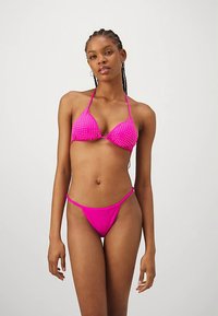 Roosa täpiline bikiinid, millel on kolmnurkse lõikega ülaosa ja minimaalne katvus alumisel osal, tehtud siledast kangast, õhukeste reguleeritavate rihmadega.