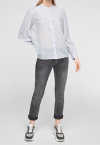 Blusa blu chiaro a maniche lunghe con chiusura a bottoni, caratterizzata da un delicato motivo, dettagli in pizzo e un design delle spalle leggermente a sbuffo.