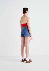 Piros nyakpántos crop top, amelyet magas derekú, szakadt farmernadrággal párosítottak. A lábbelin leopárdmintázat található lila kiemelésekkel, fehér zoknikkal.