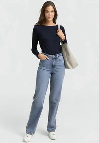 Marineblaues Langarmshirt, hellblaue, hochtaillierte Jeans und weiße Turnschuhe. Graue Tragetasche mit Henkel. Glatter Stoff, lockere Passform und gerade Schnittform.