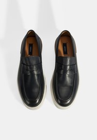 Zwarte leren instap schoenen met een ronde neus, decoratieve band en een witte rubberen zool, met een gladde textuur en minimalistisch ontwerp.