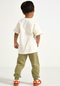 Bomuld, cremefarvet t-shirt med korte ærmer, parret med olivengrønne joggers og orange sneakers med hvide accenter og strukturerede såler.