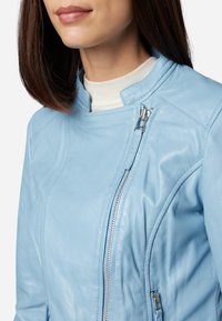 Hellblaues Lederjacke mit hohem Kragen, schrägem Reißverschluss und strukturierten Nähten. Ausgestattet mit glänzendem silbernem Zubehör und glatter Textur.