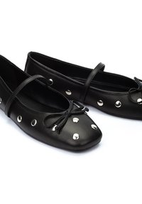 Bailarinas de piel negra con punta cuadrada, con tachuelas plateadas y un detalle de lazo. Incluyen una tira delgada a lo largo del empeine. Textura suave.