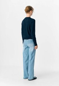 Pull à manches longues bleu marine associé à un jean large bleu clair. Le tissu semble doux, avec un design minimaliste et sans motifs visibles.