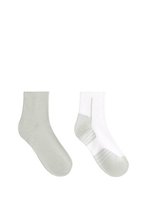 Középmagas sportzokni pár, az egyik egyszínű világosszürke, a másik fehér világosszürke sarok-, orr- és talprészletekkel, fehér háttéren bemutatva.