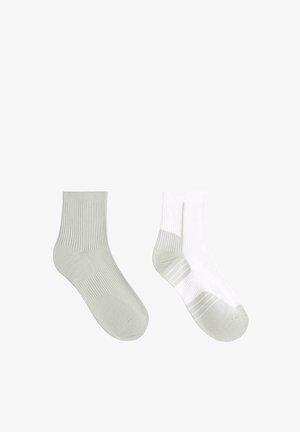 Paire de chaussettes de sport montant jusqu'au milieu du mollet, une unie gris clair et une blanche avec des accents gris clair au niveau du talon, des orteils et de la semelle, présentées sur un fond blanc.