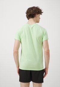 Camiseta de algodón verde claro con mangas cortas, ajuste relajado, textura suave y cuello redondo. Usada con pantalones cortos negros.