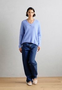Lichtblauwe v-hals trui van zacht materiaal, gecombineerd met hoge, donkerdenim jeans. Eenvoudig ontwerp, casual pasvorm en neutraal schoeisel.