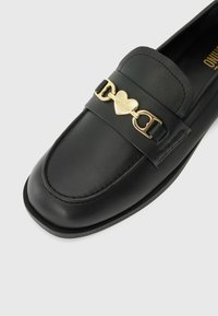 Sapatos loafers em pele preta com bico arredondado, apresentando um detalhe em corrente dourada em forma de coração e "LOVE MOSCHINO" gravado na ferragem.