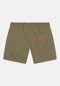 Pantalones cortos verde oliva con una cintura elástica, con un bolsillo trasero y el nombre de la marca "MADS NØRGAARD" en texto rojo.