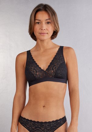 Schwarzer Spitzen-Bralette mit weichen, gewellten Kanten und einem tiefen Ausschnitt. Verfügt über ein glattes Unterband für Unterstützung. Strukturiertes Spitzenmuster auf der gesamten Fläche.