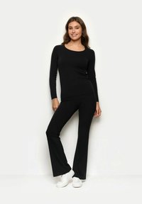 Czarny longsleeve z okrągłym dekoltem w połączeniu z czarnymi spodniami dzwonami. Oba ubrania wykonane są z miękkiego, elastycznego materiału. Uzupełnione białymi trampkami.