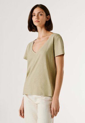 T-shirt vert olive clair en tissu doux, avec un col en V, des manches courtes et une coupe décontractée, associé à un pantalon couleur crème.