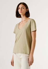 T-shirt vert olive clair en tissu doux, avec un col en V, des manches courtes et une coupe décontractée, associé à un pantalon couleur crème.