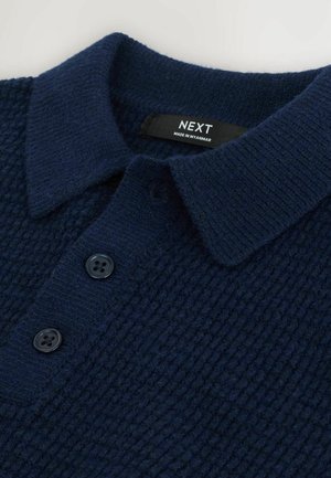 Polo shirt tricotat de culoare albastru marin, cu un material texturat, guler și trei nasturi întunecați la închidere. Eticheta este vizibilă.
