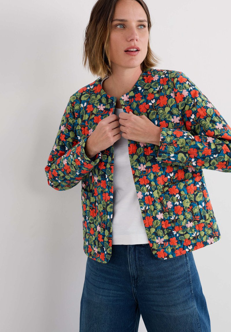 Veste matelassée en bleu marine, ornée d'un motif floral avec des accents rouges, roses et verts. Encolure ronde, manches longues et fermeture à l'avant.