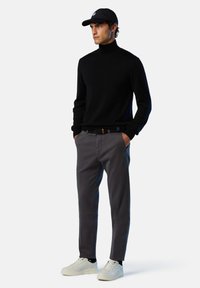 Collo nero, pantaloni grigi e sneakers bianche. Il modello indossa un cappellino nero con un logo. Maglione a maglia testurizzata e pantaloni con cintura.