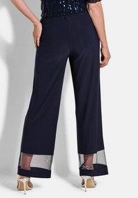 Marine wijde pantalons met een transparante mesh zoom. Zachte stof met een gladde textuur. Achteraanzicht toont een elastische tailleband en minimale details.