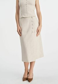 Beżowy komplet z lnu składający się z dopasowanej bluzki z guzikami z przodu i midi spódnicy z bocznym guzikiem. Połączony z brązowymi obcasami.