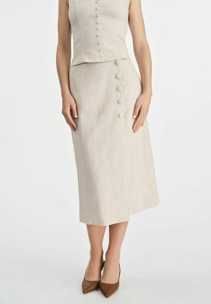 Beżowy komplet z lnu składający się z dopasowanej bluzki z guzikami z przodu i midi spódnicy z bocznym guzikiem. Połączony z brązowymi obcasami.