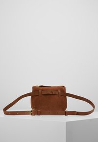 Bruine suède crossbodytas met verstelbare leren riem, ritssluiting en platte rechthoekige vorm. Heeft twee verticale accentriemen.