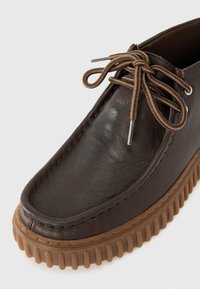 Pantof brown din piele cu talpă din cauciuc. Prezintă un vârf rotund, detalii cusute și șireturi brown. Talpa are striații texturate pentru aderență.