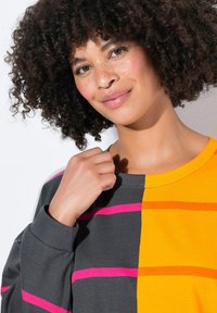 Maglietta a maniche lunghe con sezioni arancioni e grigie, con strisce rosa e arancioni. Tessuto morbido, collo tondo, vestibilità comoda, cuciture minime visibili.