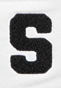 Schwarzer Plüschbuchstabe "S" mit weißem Rand auf weißem Stoffhintergrund, der eine strukturierte Oberfläche und gestickte Details aufweist.
