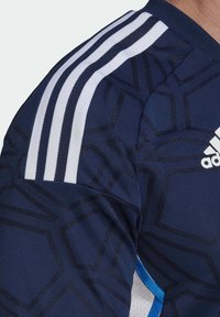 Marineblaues Sportshirt mit geometrischem Muster, weißen drei Streifen an den Schultern und blauen Akzenten. Hergestellt aus atmungsaktivem Material mit strukturierter Oberfläche.