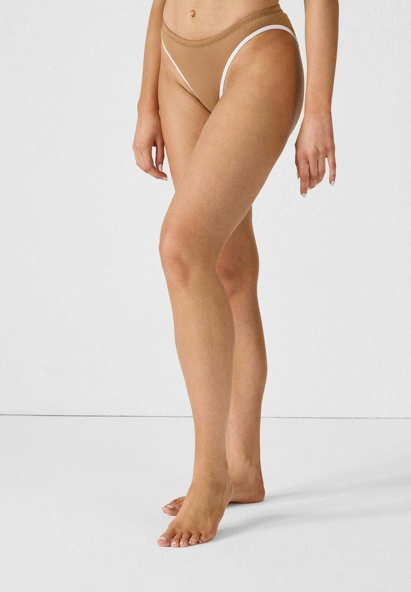 Bas de bikini tan en forme triangulaire, avec des détails en blanc. Tissu doux avec une texture lisse, conçu pour le confort.