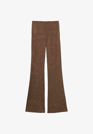 Kvinde iført en mørkebrun faux pelsjakke, brune udvidede bukser og brune åbne peep-toe hæle med pelsdetaljer mod en ensfarvet baggrund.