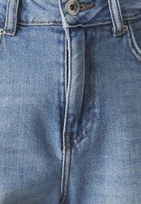 Jeans de mezclilla azul claro con diseño clásico de cinco bolsillos, cierre de botón de metal y costuras contrastantes a lo largo de las costuras.