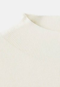 Gros plan sur un tissu tricoté crème à côtes, mettant en avant un col haut légèrement replié.