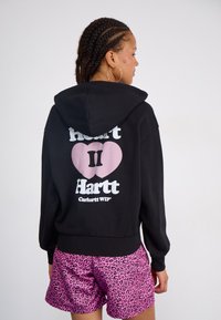 Felpa nera con una grande grafica di cuore rosa e testo, abbinata a pantaloni corti leopardati rosa. Presenta un cappuccio con coulisse e polsini a costine.