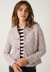 Heller rosa strukturierter Blazer mit dezentem Muster. Verfügt über silberne Knöpfe, einen Stehkragen und eine taillierte Silhouette. Kombiniert mit einem gestreiften Oberteil.